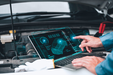 Mechanic working close to an automobile engine while using a laptop. A screen-based automotive...