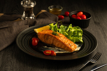 Grilled or fried salmon steak and green salad, lemon, tomato, sauce, side dish, pepper. Healthy traditional seafood with cooked fish