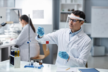 Portrait of scientist wearing protective gear and face shield in laboratory while doing experiments with chemical liquids, copy space