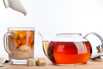 Dissolve milk in a cup of black tea. Transparent teapot and cup with three cubes of brown sugar