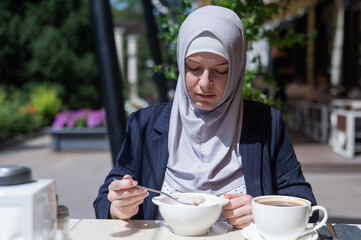 Caucasian woman in hijab having breakfast in outdoor cafe. 