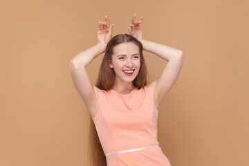 Portrait of funny smiling joyful woman with long hair standing with raised arms, showing horns,...