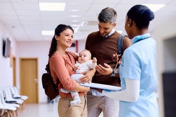 Happy parents with baby talking to pediatric nurse at medical clinic.