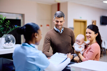 Happy parents with baby talk to reception nurse at medical clinic.