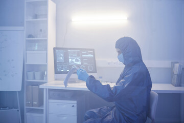 Side view portrait of scientist wearing full protective suit working at desk in biohazard dange...