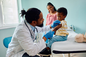 Small black boy about to get vaccinated by pediatrician at doctor's office.