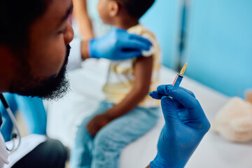Close up of black doctor preparing syringe for vaccination of child at medical clinic.