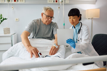 Obraz premium Hospitalize senior man and his female doctor using digital tablet at clinic.