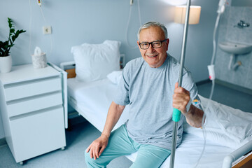 Happy senior patient with IV drip recovering in hospital and looking at camera.