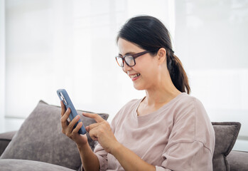 Pleasant senior mature lady resting on couch, using applications on smartphone. Happy old mature woman chatting in messenger or social network with friends or children, shopping in internet store.