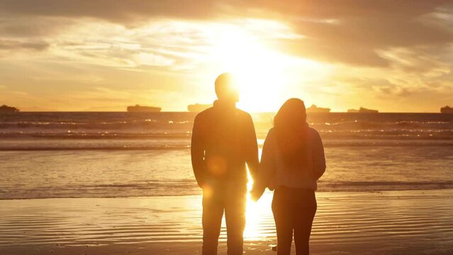 Happy couple walking on the beach at sunset.