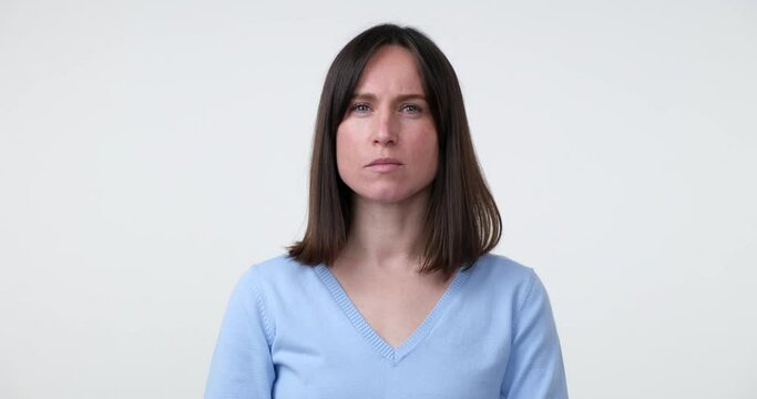 A Caucasian woman stands on a white background, making the hush gesture by placing a finger on her lips. Her face expresses seriousness and the need for secrecy.