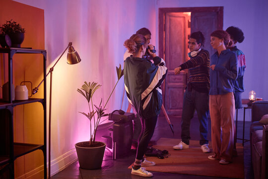 Full length view at group of young people dancing at house party with girl holding retro video camera and filming home video of friends having fun, copy space