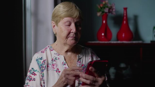 Elderly Woman Scrolling Internet on Phone by Window, Depicting Modern Technology Use at Home