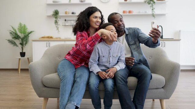 Positive african american spouses and active son having online call over cell phone held by father at home. Surprised people being involved in pleasant conversation with relatives via modern gadget.