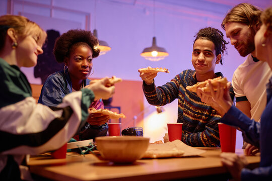 Diverse group of young people eating pizza at house party 80s style, copy space