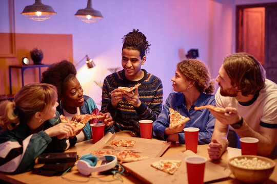 Diverse group of cheerful friends eating pizza at house party retro style, copy space