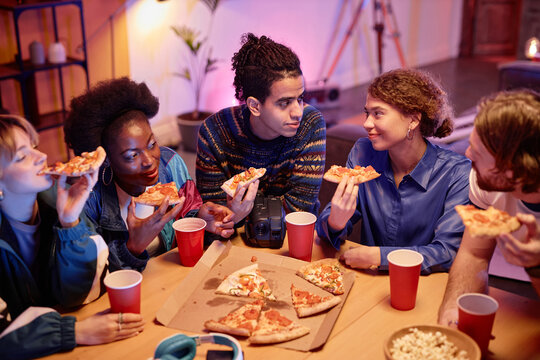 High angle view at group of young people eating pizza at house party 80s style