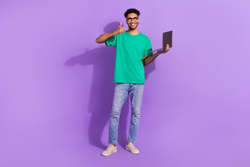 Full body photo of handsome guy hold netbook demonstrate thumb up isolated on violet color...