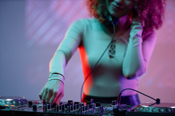 Closeup of young woman as DJ making music at turntable in neon light