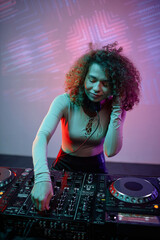 Obraz premium Vertical portrait of young woman as DJ making music tracks at disco party in neon light