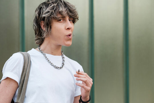 Non-binary person smoking outdoors.