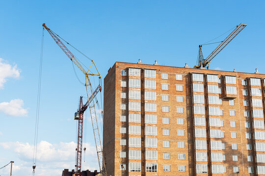 The construction of a new apartment building, against the background of the blue sky, a high-rise construction crane.