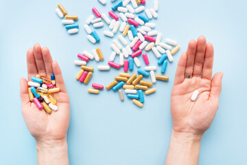 The girl holds a handful of bright vitamins in her hands, and one pill in the other, food supplements and medicines on a blue background. Concept of medicine and healthcare.