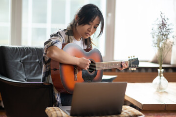 Young asian girl having an online class on playing guitar