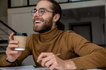 Male office worker writing in documents drinking takeaway coffee sitting at his workplace.