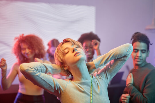 Portrait of young woman dancing with eyes closed in nightclub and enjoying mucis with crowd in background