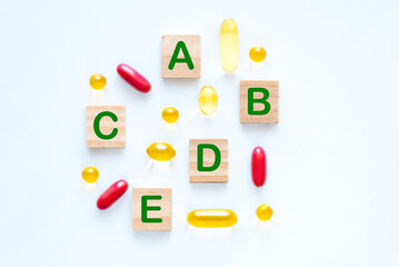 Set of capsules of different vitamins and letters on wooden blocks on white background flat lay. Healthy lifestyle concept
