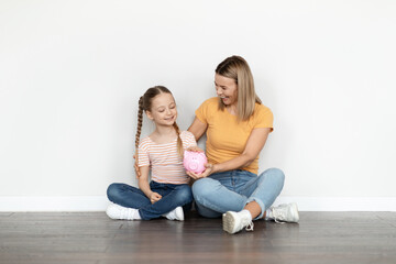 Fototapeta na wymiar Family Savings. Happy Young Mother And Cute Little Girl Holding Piggy Bank