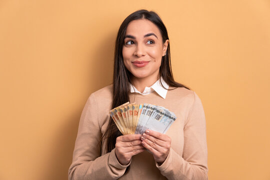cheerful brazilian woman with money, brazilian real in beige studio background. finance, investment, offer, loan concept. 