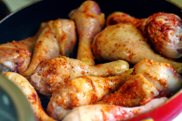 Chicken drumsticks with hot red spices are fried in a frying pan