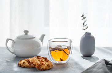 A glass of herbal tea, teapot and homemade cookies on the background of a window with morning...