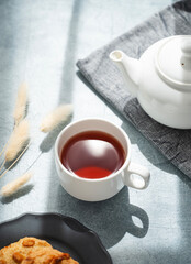 A cup of fragrant tea with homemade cookies and a white teapot on a blue background in the morning sunlight. Delicious breakfast concept.