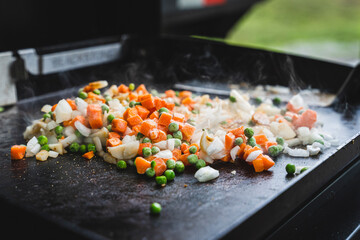 Peas, carrots, and onion cooking on a griddle outside in a campsite