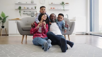 Energetic multiethnic children in jeans clothes talking to relaxed adults while staying indoors on sunny day. Adorable brothers asking joyful parents about stroll after meals in park outside.