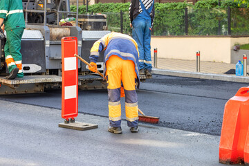 A team of road builders on an asphalt paver carefully lay fresh asphalt on the carriageway.