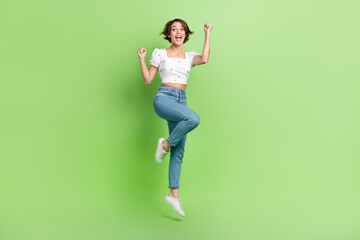 Fototapeta na wymiar Full length photo of delighted carefree person jumping raise fists empty space isolated on green color background