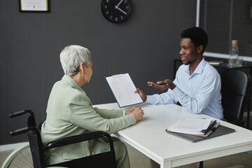 Portrait of smiling HR recruiter speaking to senior woman with disability in job interview