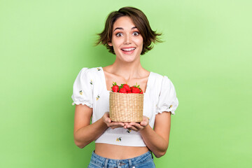 Photo of excited funky woman dressed white top holding strawberries basket isolated green color...