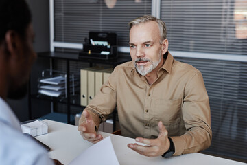 Portrait of bearded mature man speaking to recruiter during job interview