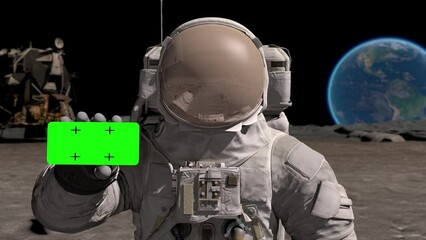 Astronaut on Moon wearing helmet shows a smartphone with a green screen. Sci-fi expedition, planet discovery mission and exploration by brave human, spacewalk. Green screen chroma key.