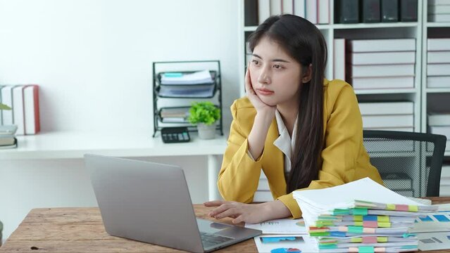 Young Asian business woman employee showing boredom and exhaustion from thinking working on paperwork and computer in office, burnout syndrome, tired, worried concepts