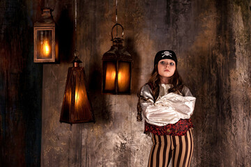 Portrait of little girl in pirate's image 7-8 year old posing at grey textured wall with lamps,...