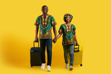 Happy excited african couple tourists carrying luggages on yellow