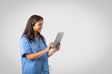 Telemedicine concept. Cheerful senior woman doctor with tablet and headset making online consultation, free space