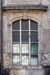Rectangular cellular arched window with opaque glass against the background of an old weathered stone wall with a downpipe. From the Windows of the world series.